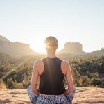 Lotus Sunrise - Back view of anonymous fit woman in comfortable summer wear sitting in Padmasana and meditating on sunlit cliff at sunrise
