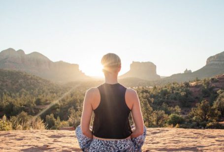 Lotus Sunrise - Back view of anonymous fit woman in comfortable summer wear sitting in Padmasana and meditating on sunlit cliff at sunrise