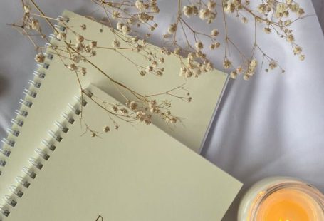 Candle Book - Top view composition of white spiral copybooks with inscription Do What You Want placed on white cloth with burning candle and tender flower