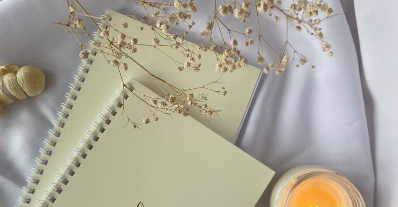 Candle Book - Top view composition of white spiral copybooks with inscription Do What You Want placed on white cloth with burning candle and tender flower