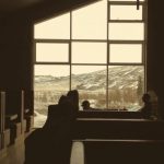 Ceiling Break - Dark brown tables and couches under angled ceiling in empty dark cafe with mountain through big window