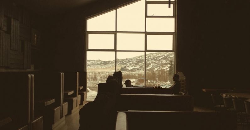 Ceiling Break - Dark brown tables and couches under angled ceiling in empty dark cafe with mountain through big window