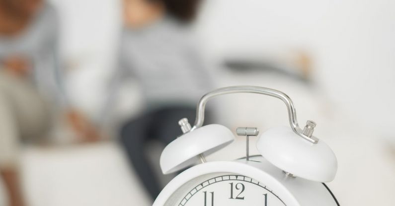 Clock Generations - Retro styled alarm clock placed on table in bedroom near unrecognizable African American little child playing with mother
