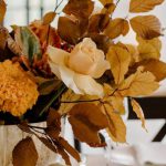 Fork Leaf - Elegant floral composition in vase placed on white table with ceramic plates and golden cutlery during festive banquet